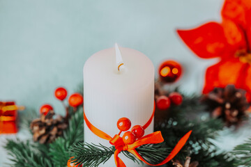 White candle with orange ribbon decorated with pine cones and red berries on a blue background