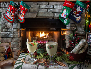 Obraz premium Two glasses of creamy holiday drinks sit on a table near a warm fireplace. Christmas stockings hang above, and decorations create a cozy atmosphere filled with cheer during the festive season.