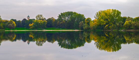 Panorama of symmetrical landscape by lake with trees reflected in water mirror