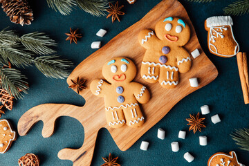 Two gingerbread men cookies sit on a wooden board with festive holiday decorations and spices.