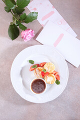 Cheesecakes with strawberries and jam. Healthy breakfast. A menu page and a rose on the table. View from above.