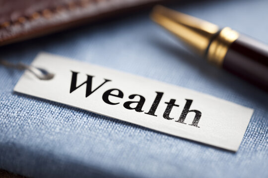 "Wealth" handwritten on a notepad with a fountain pen, watch, and dollar sign nearby, symbolizing financial planning, time management, and wealth goals.