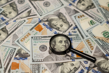 Detailed Examination of Hundred Dollar Bills With a Magnifying Glass on a Surface Covered in Cash