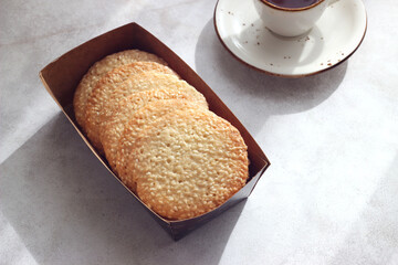 Sesame cookies in a box on the table, next to a cup of black tea