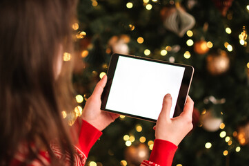 Woman in a red sweater holding a blank screen tablet for mockup against a blurred Christmas tree background with golden lights.