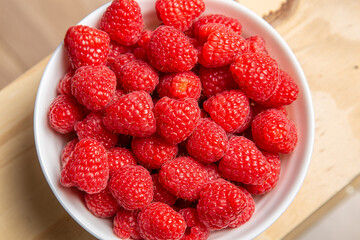 Top-down view, filling the frame, of fresh vibrant red raspberries in a white bowl
