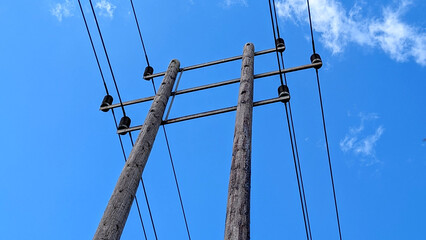 Wooden electricity telegraph poles carrying power lines against a clear blue summer sky