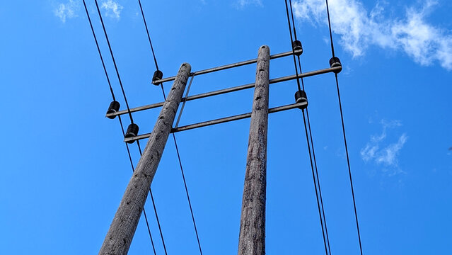 Wooden electricity telegraph poles carrying power lines against a clear blue summer sky