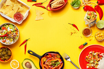 Set of traditional mexican dishes - burrito wraps, nachos, burrito bowl and fajitas in cast iron pan on yellow background with vegetables and sauces. Top view, flat lay, copy space, frame composition