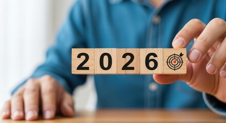 Hand holding wooden blocks with the year 2026 and a target symbol