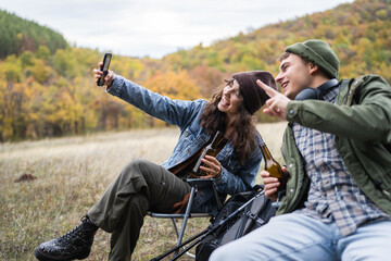 Happy young couple enjoying autumn nature taking selfie with beer