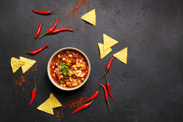 Traditional mexican dish chili con carne in ceramic bowl on black concrete background with chili peppers and nachos. Overhead view, flat lay, copy space. Minimal abstract composition