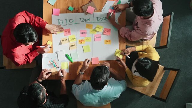 Top view of people writing and making scrum task board while writing marketing and planning strategy at colorful sticky notes. Smart team manage work performance by using kanaban board. Convocation.