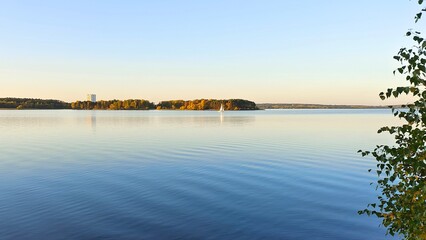 Birches with yellow leaves grow on the shore of the lake. A sailing yacht is floating. There are...