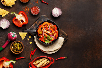 Traditional mexican dish fajitas in cast iron pan with tortilla, nachos, grilled corn cobs, vegetables, sauces and maracas on dark concrete background. Flat lay, overhead view, copy space