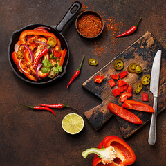 Traditional mexican dish fajitas in cast iron pan with ingredients for cooking on dark concrete background. Flat lay, overhead view