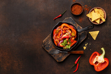 Traditional mexican dish fajitas in cast iron pan on vintage wooden board with nachos and vegetables over dark concrete background. Flat lay, overhead view, copy space