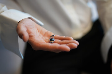 The groom holds his shirt cufflinks in his hand.
