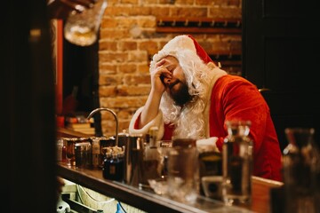 Overworked santa claus resting head on hand at bar