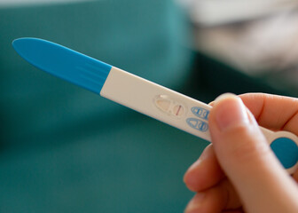 Close-up of a hand holding a pregnancy test with a visible result.