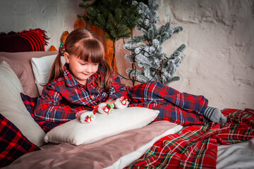 Happy little girl child in pajamas lies in bed in bedroom. Christmas. New Year. St. Nicholas Day. Time of holidays and miracles.	