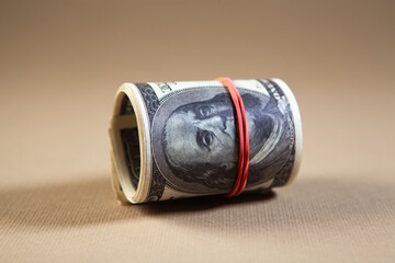 Roll of one hundred dollar bills tied with red ribbon on a brown background