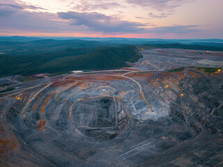 Aerial view of vast gold ore open pit mine during stunning sunset over lush mountain landscape