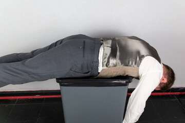 Vintage Businessman Dangling Limply Atop a Garbage Can. Concept of Being Sacked or Fired. Stock Market Crash.