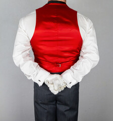 Butler or Hotel Concierge in Red Vest or Waistcoat and White Gloves Standing With Hands Behind His Back. 
