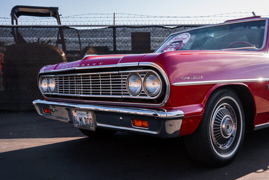 A red Chevrolet Chevelle convertible sits in an industrial lot in Monterey, California, low three quarter front view, chrome details gleam in late afternoon light.