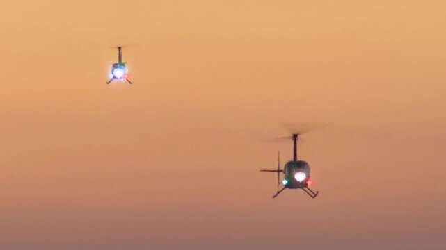 Twin helicopters landing in sequence at an airport helipad in the California dusk.