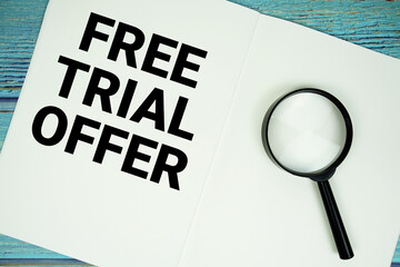 Free Trial Offer text written on notepad with magnifying glass flat lay on wooden background