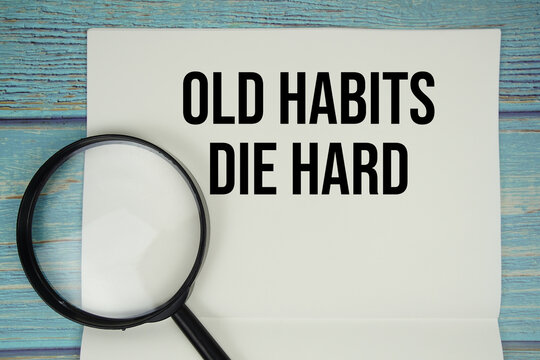 Old Habits Die Hard text written on notepad with magnifying glass flat lay on wooden background