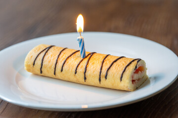 Close-Up of Mini Strawberry Roll Cake and Birthday Cake with a Burning Candle on a White Plate
