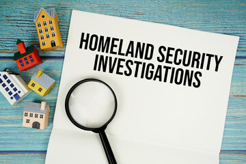Notepad with "HSI Homeland Security Investigations" with magnifying glass and house model on wooden background