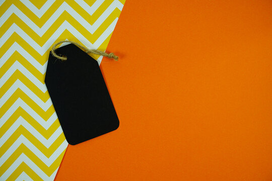 Gift tag with twine resting on orange and yellow chevron background for Halloween labels, price tags, or seasonal promotions with space for custom text.