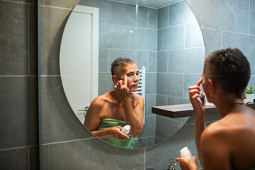 Mature woman applying skincare in bathroom