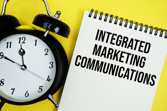 Integrated marketing communications text with alarm clock flat lay on yellow background