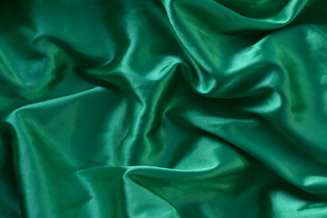 Fototapeta premium A closeup minimalist textured pattern. Green satin fabric texture luxurious shiny. Background with pattern soft waves blur beautiful.