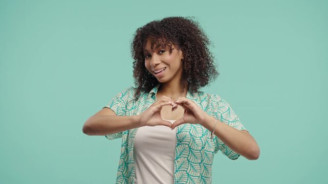 Pretty woman forms heart shape with hands, sending love. Charming teenage girl on blue background. Women health, volunteering, charity donation, gratitude symbol, flirting