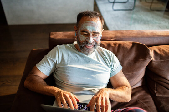 Mature man with face mask using laptop at home