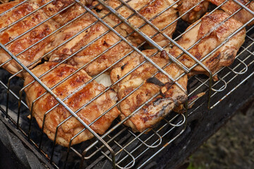 Juicy pieces of chicken are grilled in a metal grill over hot coals. The ruddy crust and smoky aroma emphasize the atmosphere of a picnic and a summer vacation in nature.