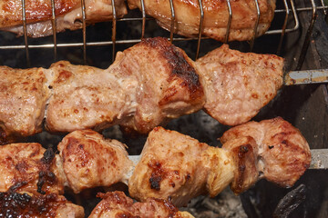 Large pieces of pork being grilled on skewers over hot charcoal. Delicious barbecue with a golden crust cooking outdoors during a picnic or countryside gathering.