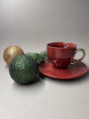 Red cup of coffee with gold and green Christmas baubles and fir branch on neutral background