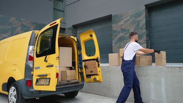Delivery man unloading cardboard boxes from yellow van near warehouse