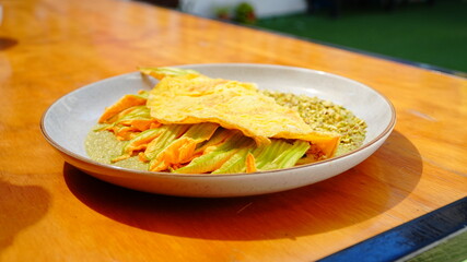 Platillo servido en plato artesanal con una omelette dorada acompañada de flor de calabaza y salsa verde.