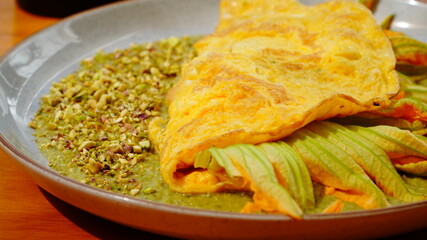 Platillo servido en plato artesanal con una omelette dorada acompañada de flor de calabaza y salsa verde.