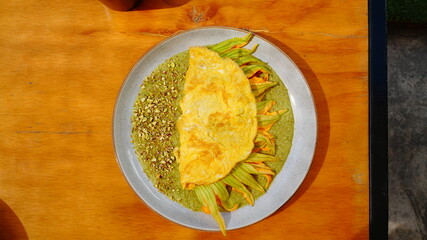 Platillo servido en plato artesanal con una omelette dorada acompañada de flor de calabaza y salsa verde.
