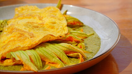 Platillo servido en plato artesanal con una omelette dorada acompañada de flor de calabaza y salsa verde.