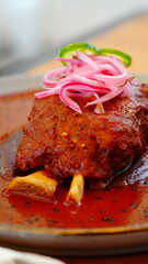 Platillo tradicional mexicano bañado en salsa roja, decorado con cebolla morada encurtida y rodajas de chile verde.